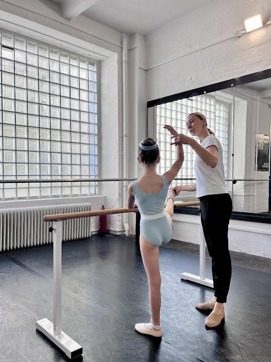 Anastasia correcting a young student's arm position at the barre